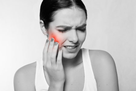 Photo of a woman grimacing in toothache pain while holding her cheek.